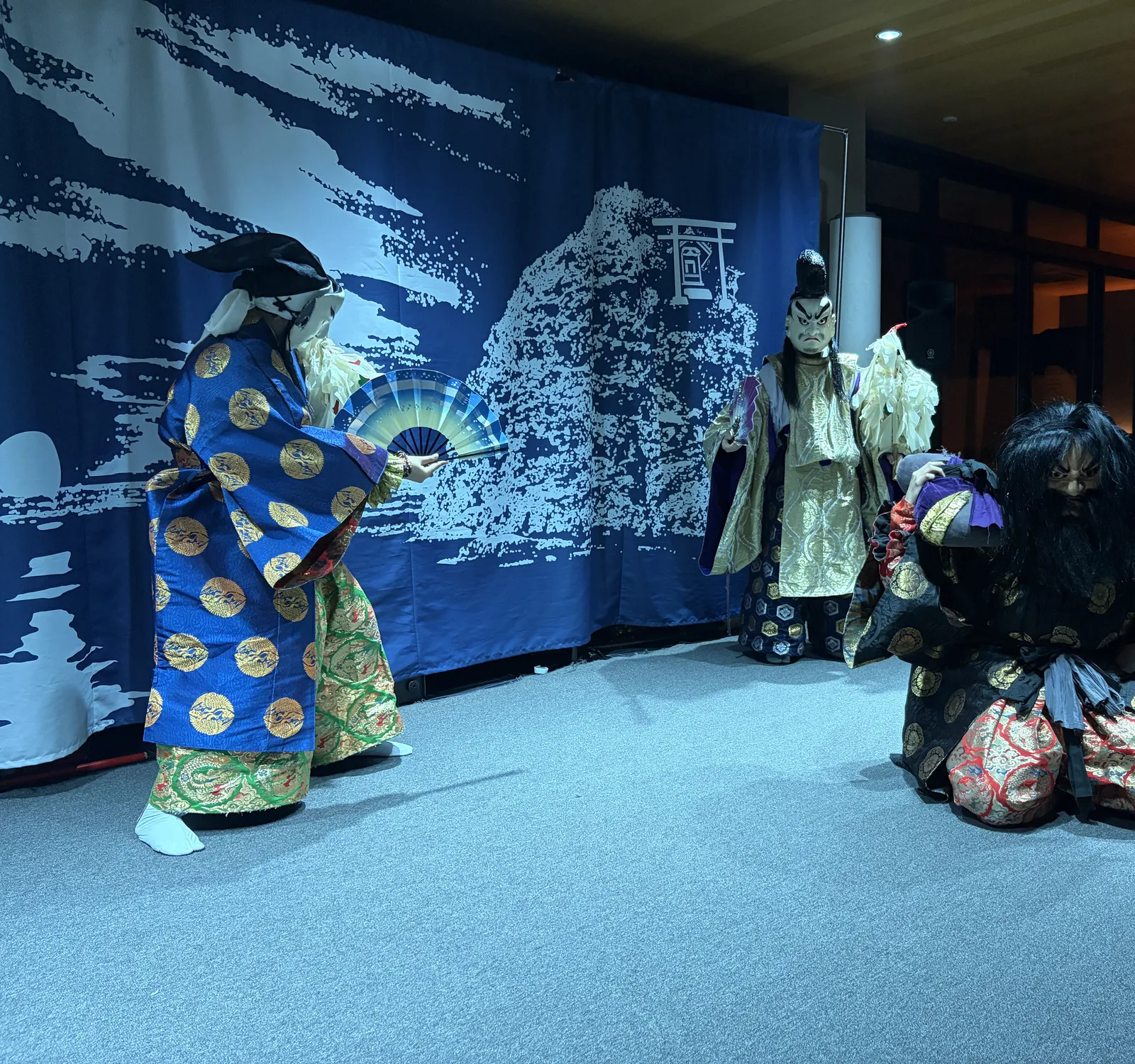 青い幕の前で、豪華な衣装と面を着けて舞う石見神楽の演者