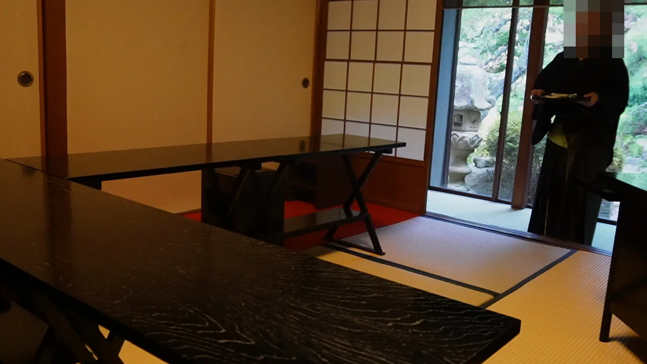 畳敷きの茶室と黒い座卓、奥に庭が見える窓